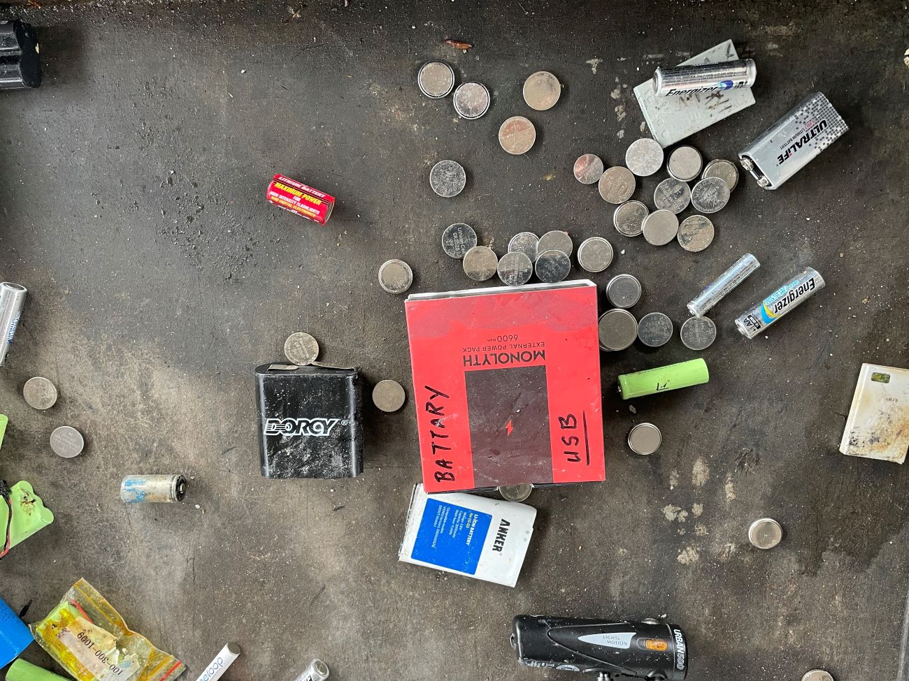 Various small batteries scattered on a table, including a bright red square battery, many loose round nickel batteries
