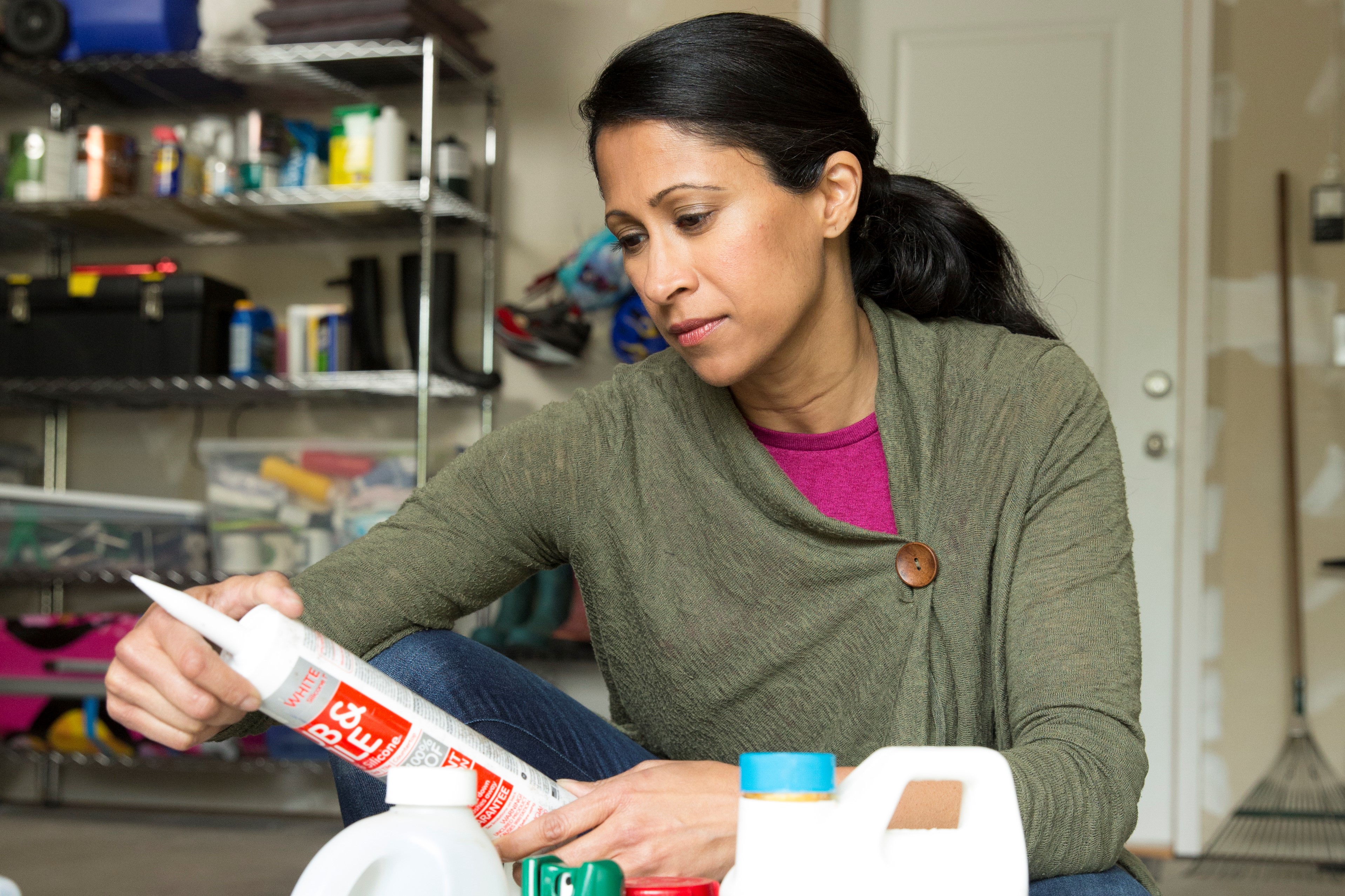 A woman in her garage reads the label on a tube of caulk