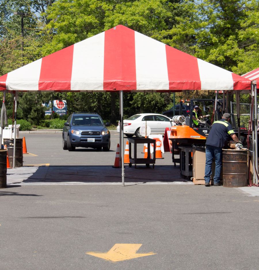 A red and white tent stands in a parking lot with tables set up underneath collecting hazardous waste at the Wastemobile 